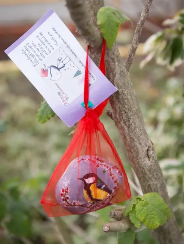 A painted stone hanging in a gift bag on a tree