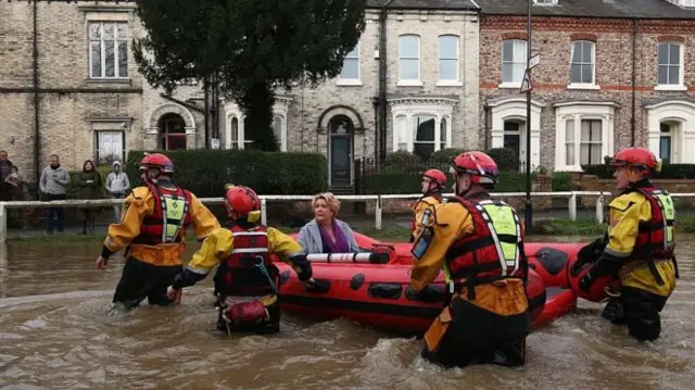 Rescuers with a dingy taking a woman from her home during flooding