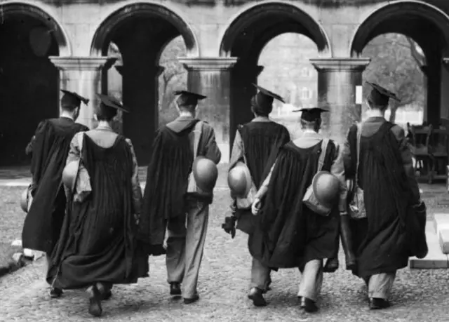 Cambridge undergraduate members of the University fire squad in cap and gown carrying their gas masks and tin helmets so as to be ready for any emergency