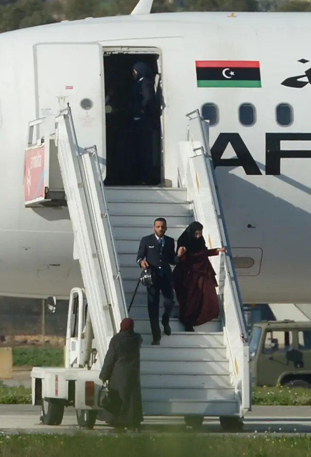 A picture taken on December 23, 2016 in Valletta, Malta, shows a crew member helping one of the hostages to disembark from the Afriqiyah Airways A320 after it was hijacked from Libya