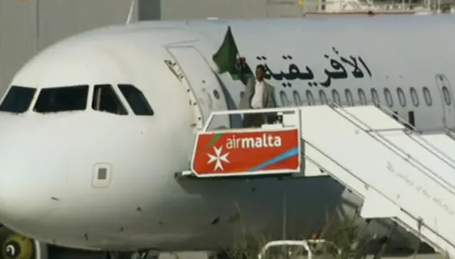 An Afriqiyah Airways plane stands on the tarmac at Malta International airport as an unidentified man waves a flag