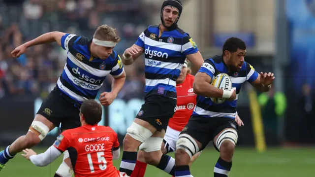 Taulupe Faletau (R) of Bath avoids the challenge from Alex Goode of Saracens as Tom Ellis lends support