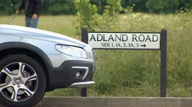 Road sign for Adland Road, and the front of a vehicle
