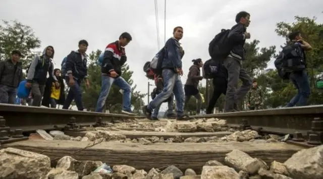 Syrian refugees walking along rail track