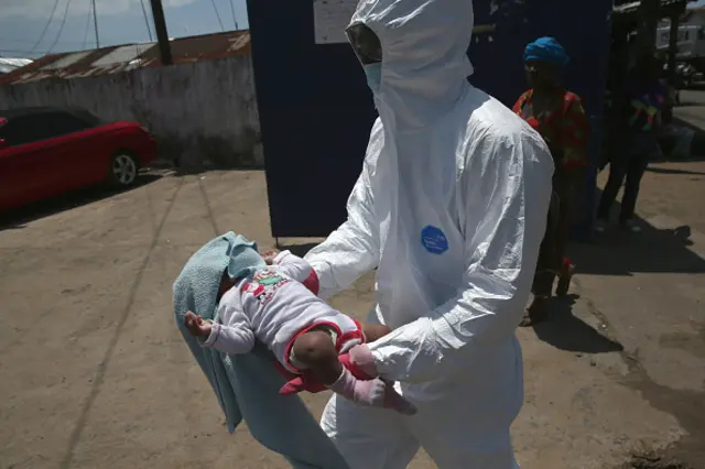 A health worker carries Benson, 2 months, to a re-opened Ebola holding center in the West Point neighborhood on October 17, 2014 in Monrovia, Liberia