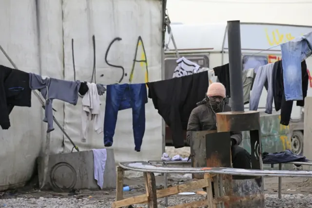 A migrant from Sudan tries to warm up in the migrant camp in Calais known as "the Jungle", France