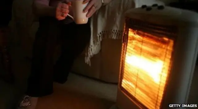 Woman sitting beside electric fire with a cup of tea