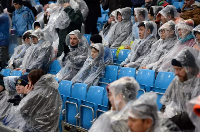 Football supporters wear waterproofs before the English Premier League football match between Manchester City and Leicester City at the Etihad Stadium