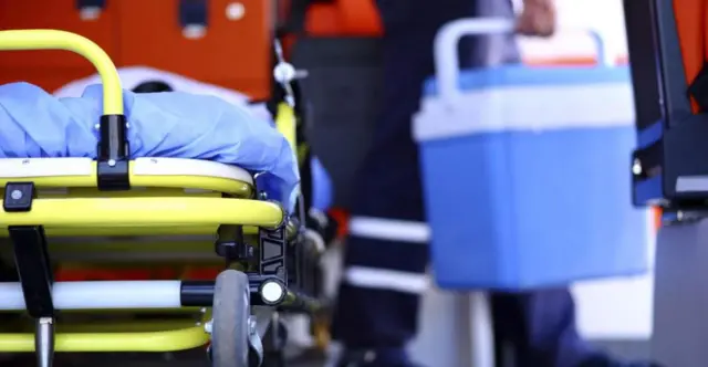 Man carrying organ donation box with a gurney in the background