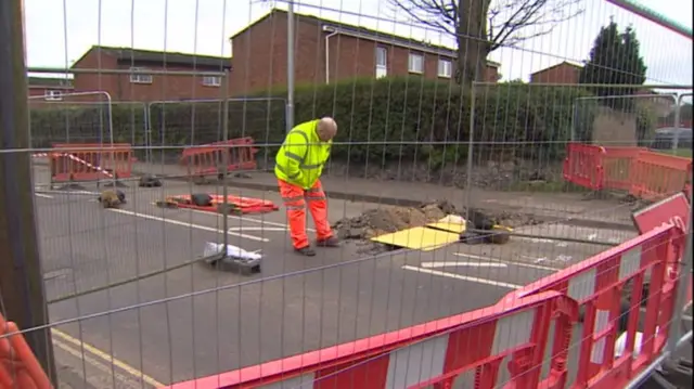 Plumstead Road, with barriers around the sinkhole, and a workman looking in