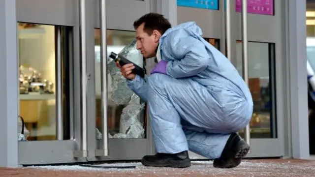 A police forensics officer examines the shattered front doors of the shopping centre