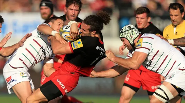 Mike Ellery of Saracens is tackled by Fergus Mulchrone and Chris Noakes of London Irish