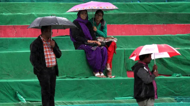 Spectators shelter under umbrellas