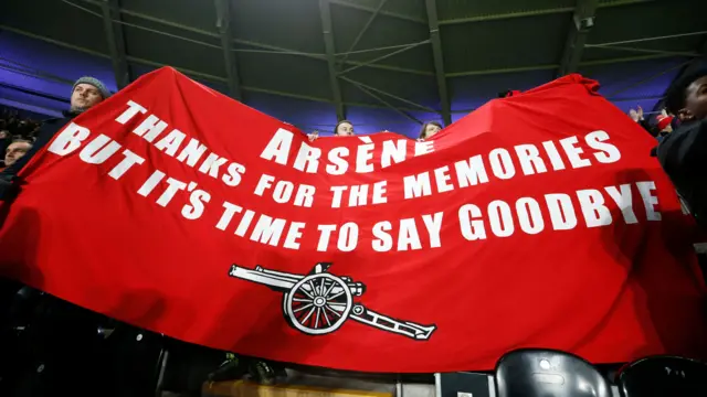 Fans hold up a banner protesting against Arsene Wenger