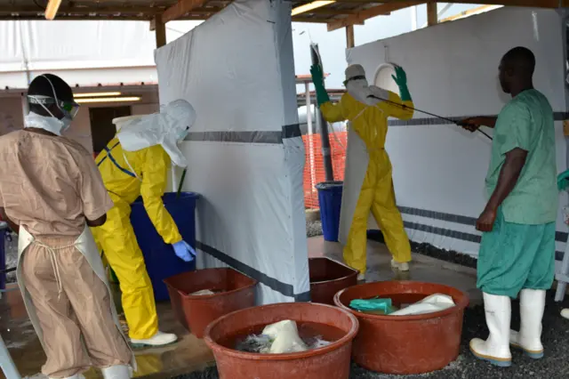 A health worker wearing protective gear is sprayed with disinfectant at the Nongo ebola treatment centre in Conakry, Guinea, on August 21, 2015.