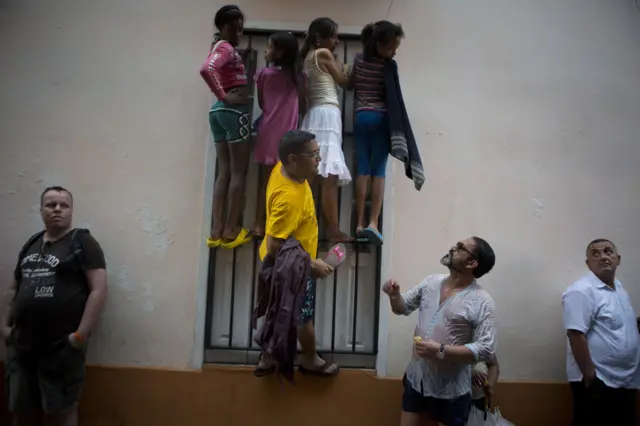 People climb a window grate as it rains in hopes of catching a glimpse of President Barack Obama