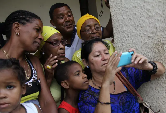 Cuban citizens look on a mobile phone at a broadcast of the US President Barack Obama's arrival in Havana