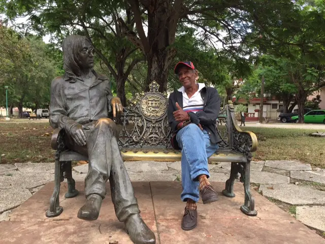 Luis sits next to John Lennon statue