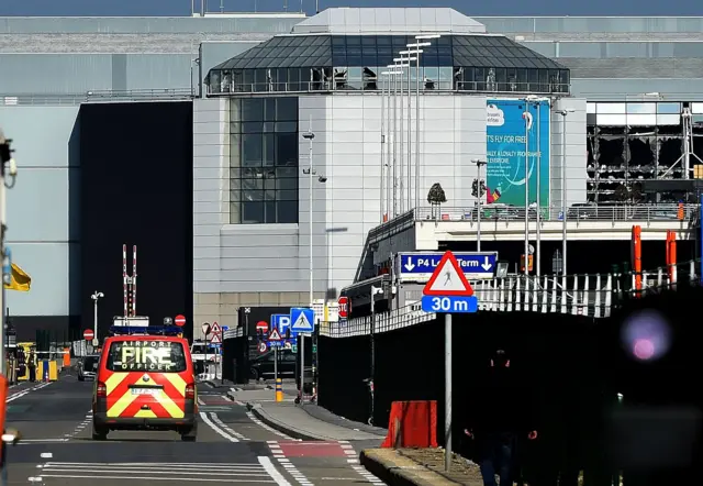 An airport fire brigade car is seen driving near the shattered glass facade of the departure hall at Brussels Airport in Zavedam