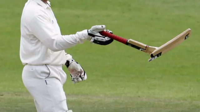 A cricketer holds a broken bat