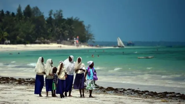 Women walk along a beach in Zanzibar