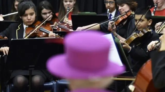 Queen Elizabeth II watches the National Youth Orchestra of Great Britain perform during her visit to Lister Community School