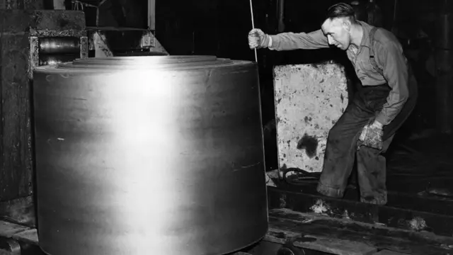 A worker in 1961 measures a roll of steel