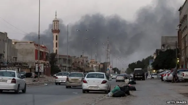 Benghazi with cars on the road and smoke in the background