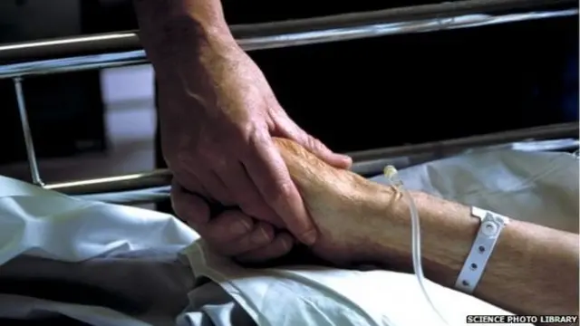 Woman in hospital bed holding man's hand