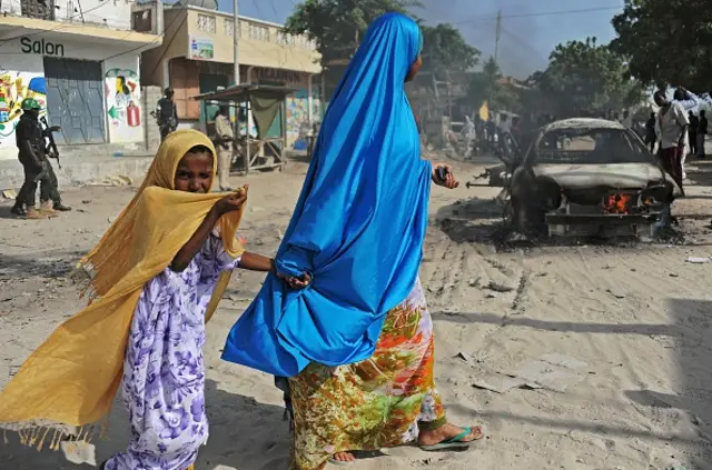 A mother and a child walk past the wreckage of a car bomb in the Wardhigley District, south of Mogadishu, on February 27, 2015.