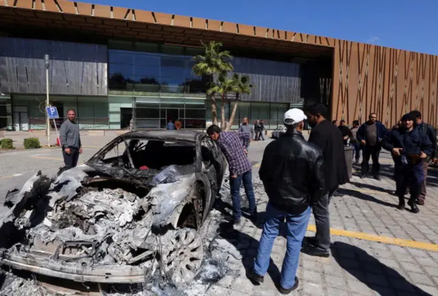 Libyan men inspect the wreckage of a car in front of the General National Congress (GNC) in Tripoli on March 3, 2014 after dozens of protesters stormed the parliament and wounded two of its members