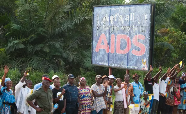 Cameroon's residents wave to the convoy of Pope Benedict XVI under a sign reading 'aids', from Yaounde airport to downtown Yaounde on March 17, 2009.