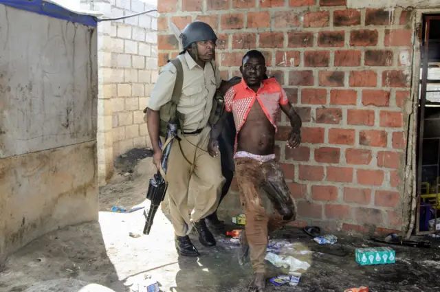 A Zambian Policeman apprehends an alleged looter in the Zingalume Compound where residents have attacked broken and looted foreign-run shops in Lusaka on April 18, 2016