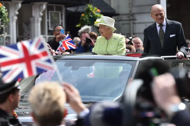 Queen and Prince Philip greet crowds from an open-top car