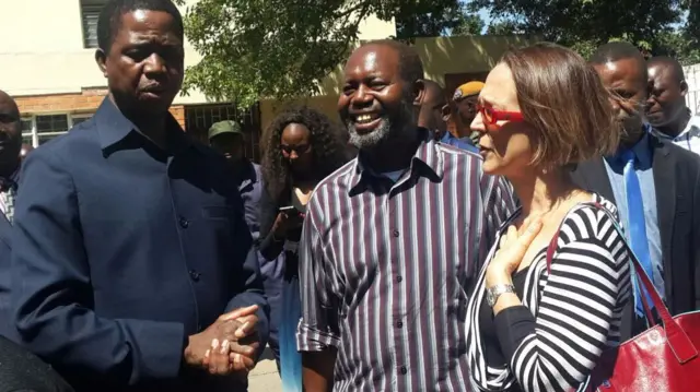 Zambian President Egar Lungu (L) with Catholic priest Fr Charles Chilinda (C) and UNHCR country representative Laura Locastro (R)