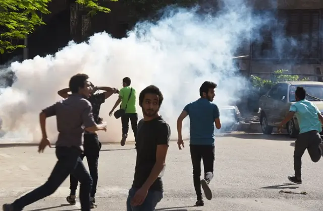 Egyptian protesters run for cover from tear gas fired by riot police during a demonstration in Cairo on April 25, 2016