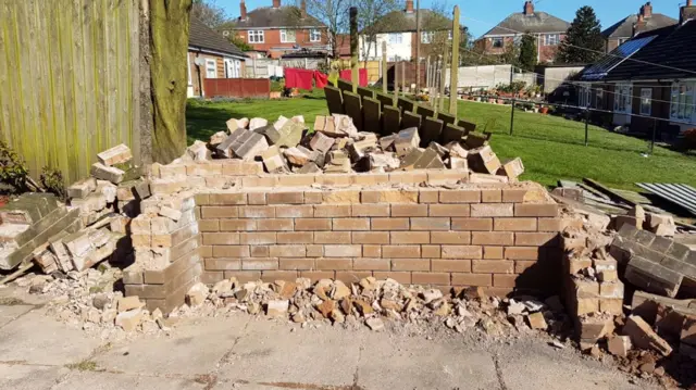 A wall with dozens of bricks lying about it after high winds