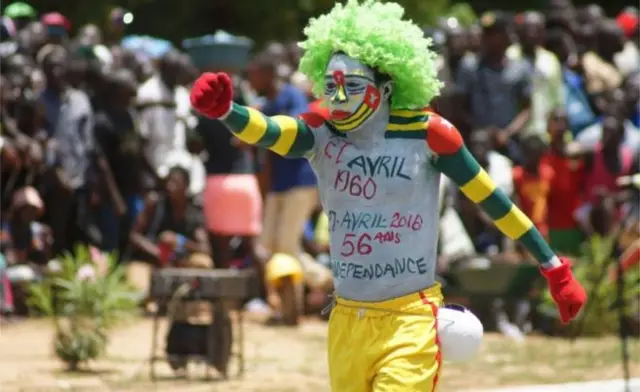 Man in yellow trousers with facepaint, a curly green wig and