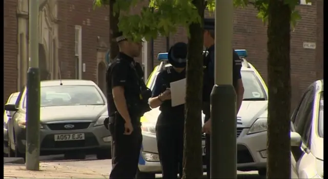 Three police officers in the street, with vehicles