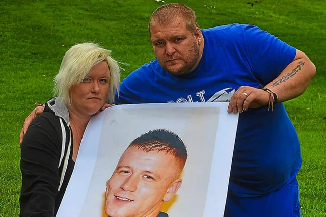 Charlotte Delo with her husband Delwyn, holding a picture of Charlotte’s brother Jamie Penn