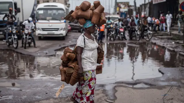 A woman carrying baskets crosses a street in the Matonge district, Kinshasa, DR Congo