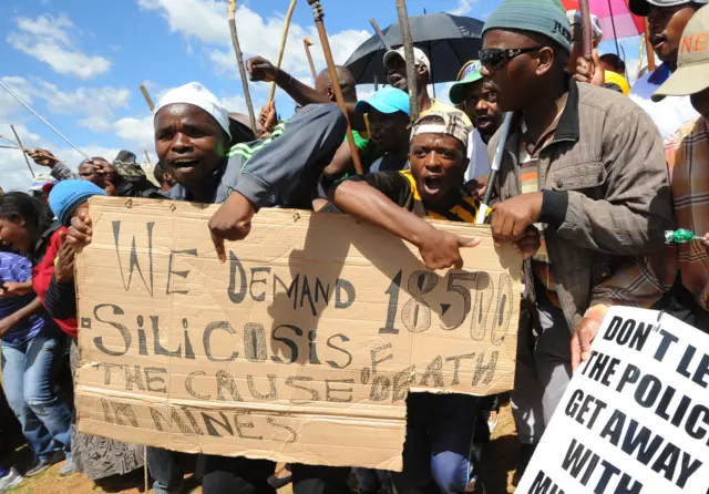 Miners in South Africa holding a sign about silicosis