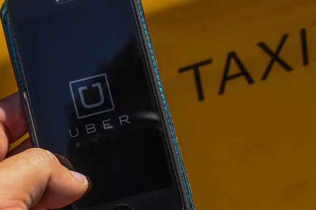 In this photo illustration, the new smart phone app 'Uber' logo is displayed on a mobile phone next to a taxi on July 1, 2014 in Barcelona, Spain