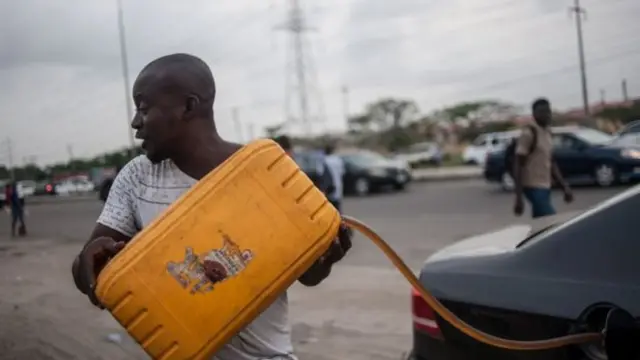 Man fills jerry can with petrol from car