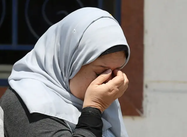 woman in grey headscarf - face not visible as she has her hands to her eyes. May 19, 2015