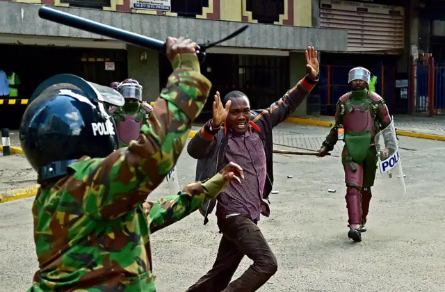 Kenyan riot police officers raise batons over a man during a demonstration of Kenya's opposition supporters in Nairobi, on May 16, 2016