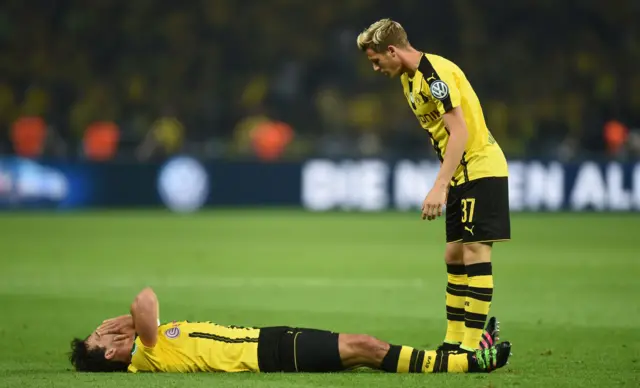 Erik Durm (R) stands next to Dortmund"s defender Mats Hummels who lays on the pitch and grimaces in pain