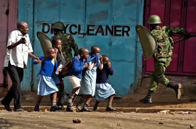 Kenyan police run past a group of children during protests in Kisumu