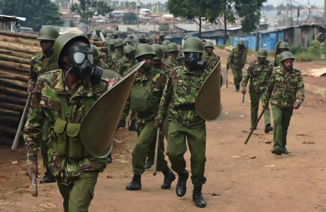 Police in gas masks walk through the Kibera slum