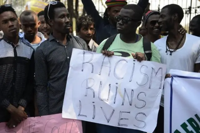 Nigerians in India hold sign saying "Racism ruins lives"